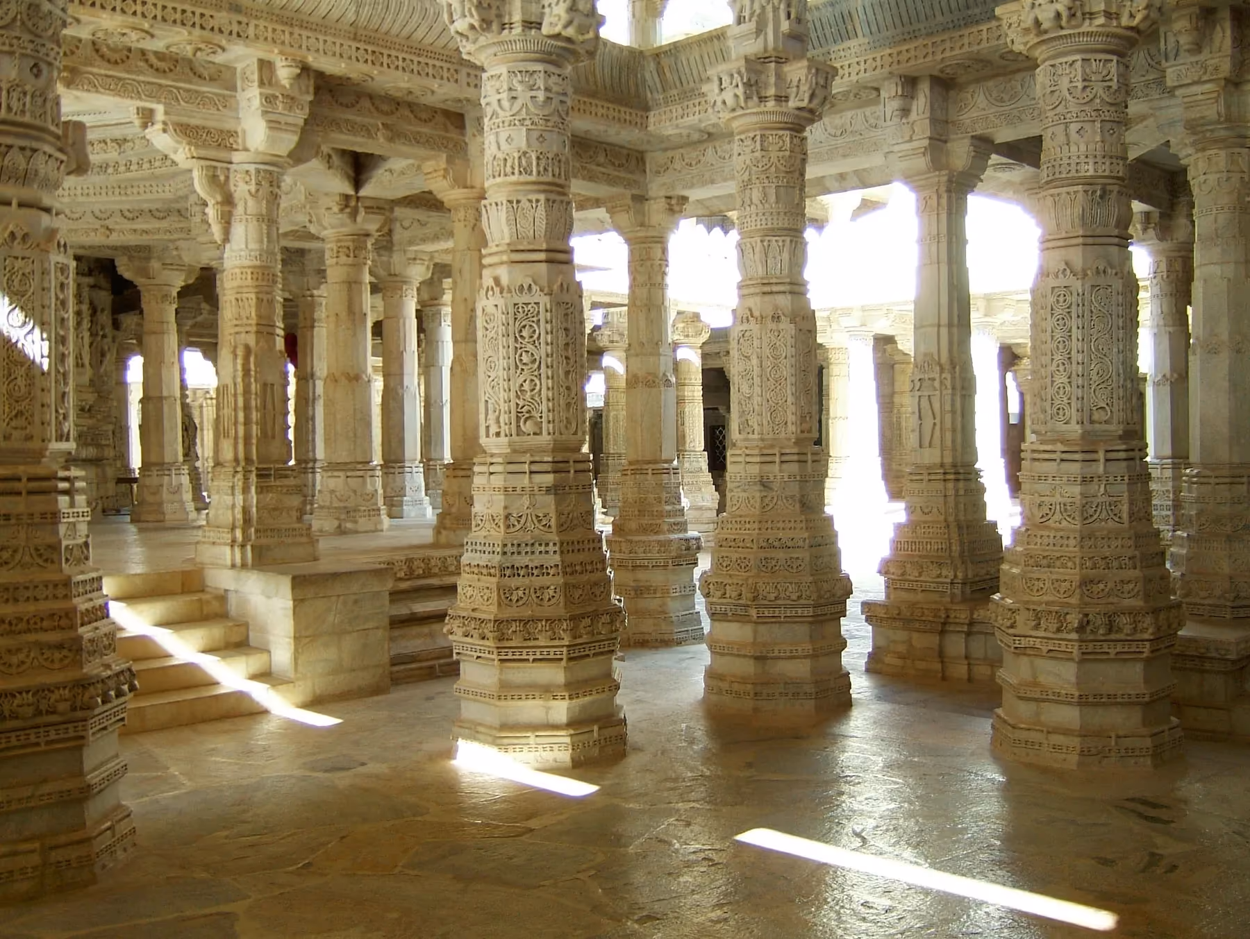 Marble pillars and carved panels inside the Ranakpur Jain temple, lit by daylight from the open courtyard